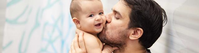 Homem sentado beijando as bochechas de um bebê
