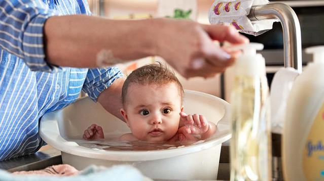 Bebê tomando banho numa banheira ao lado de produtos Johnson's baby