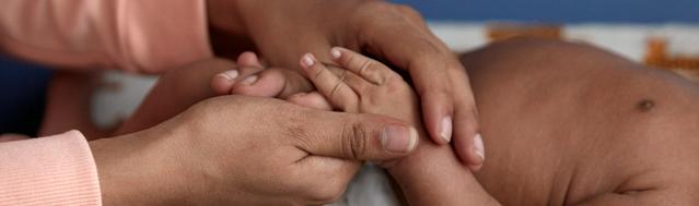 Mãe segurando com as duas mãos a mão do recém-nascido