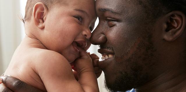 Homem sorrindo ao segurar bebê próximo do rosto 