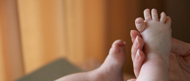 Mãos de um adulto segurando o pé do bebê